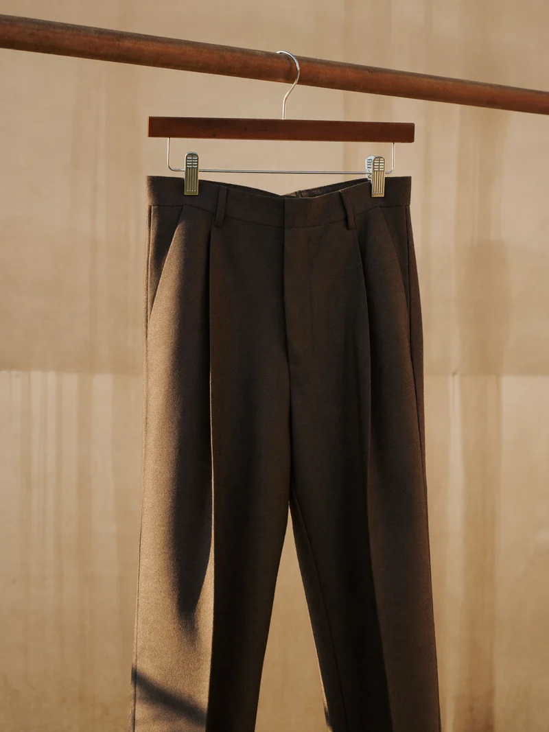 Anthrazitfarbene Hose mit hohem Bund an einer Kleiderstange vor Putzwand